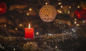 Foto de una vela solitaria entre la decoración navideña, representando la soledad del duelo en Navidad.